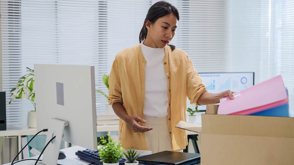 In an office setting, a woman packs a box with office supplies. The image accompanies the text "Setting Up Emergency Planning and Cash Flow."